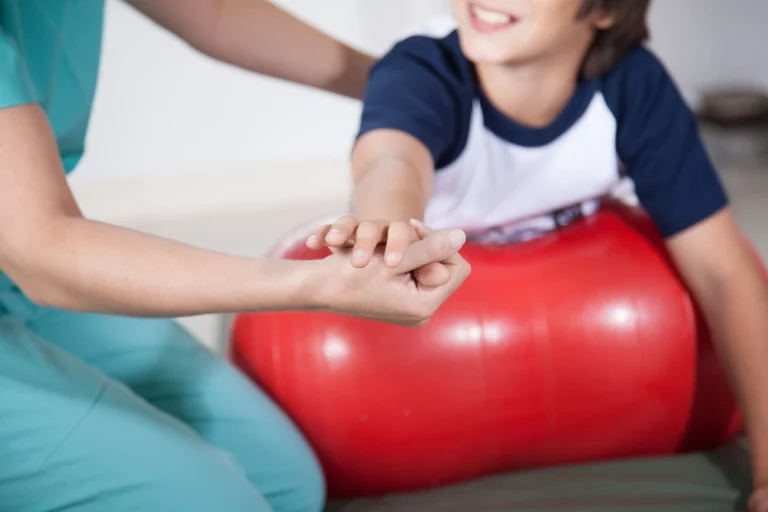 The YBL CATT physiotherapist is holding a child participant’s hands to support him during therapy